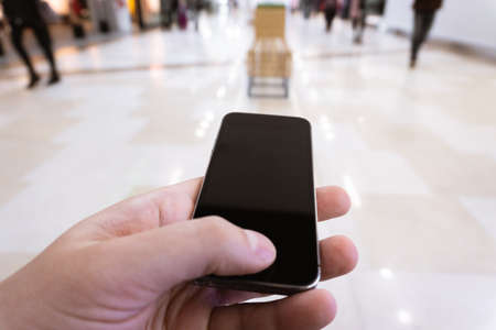 male hand holding a smart phone in a shopping center the concept of managing people with phone