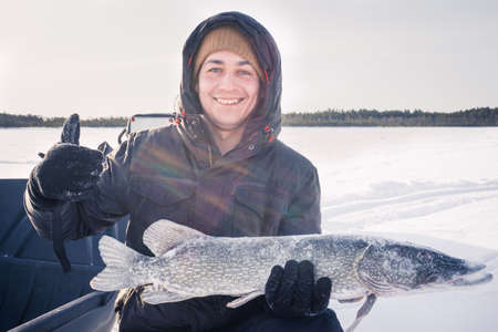 young man holding fish catch a big pike ice fishing