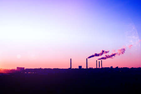 Factory pipe polluting air, environmental problems, ecology theme, the smoke from the chimneys. purple sunset on the background of the cityの写真素材