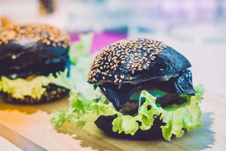 Big black sandwich, hamburger or burger with beef or chicken, tomatoes, cheese, lettuce and a sesame bun on a paper on a wooden tableの写真素材