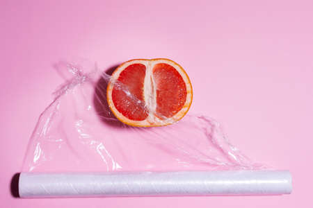 wrapping plastic transparent food film on pink background packaging of citrus fruits, grapefruit. place for text, top viewの写真素材
