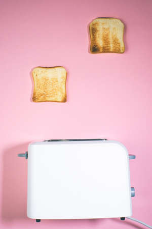 Roasted bread jump out from a white toaster. close-up view of pastries in process a toasting deviceの写真素材