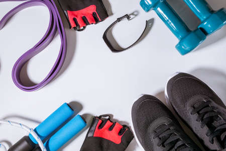 sport background with sneakers, measurement tape, dumbbells, jump rope, gloves, fitness tracker, elastic expander on ankles flat lay white background with copy spaceの写真素材