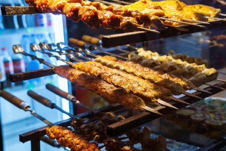 kababs are being grilled with heat in barbeque with metal skewers, at evening for sale as street foodの写真素材