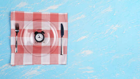 Concept of intermittent fasting, diet and weight loss. Plate as Alarm clock on blue backgroundの写真素材