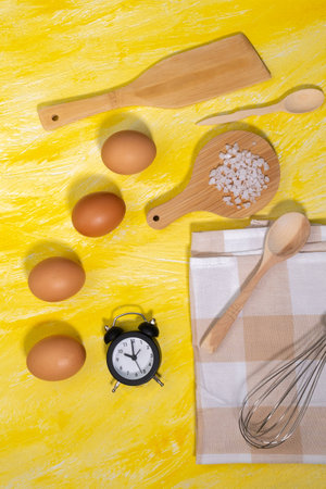 Wooden kitchen utensils eggs, sea salt, mixer. cooking food top view on a yellow background. vertical photoの写真素材