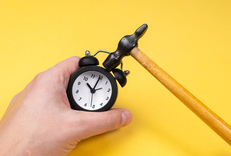 alarm clock with a hammer on a yellow background. the destruction of time. space for textの写真素材