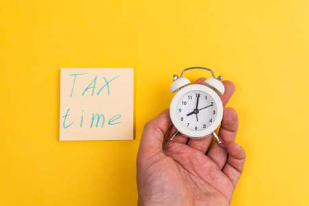 Tax time written with an alarm clock on yellow background. Tax payment reminder or annual taxation concept.の写真素材