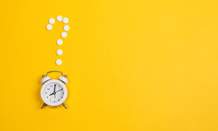 Contraception Day contraceptive pills with alarm clock on yellow background.の写真素材