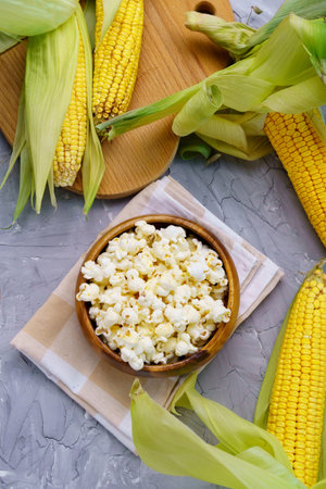 A bowl with delicious traditional popcorn and corn cobs on a gray background. Vertical photoの写真素材