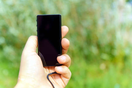 A man listens to music in an mp3 player. He holds a gadget in his hand, in nature.
