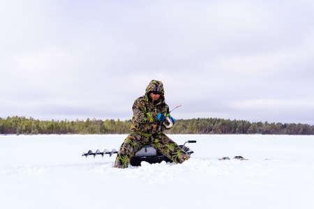 Ice fisherman on the lake catches perch during winter fishing. Space for copying text