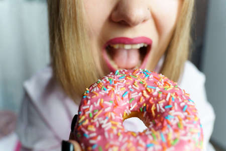 Young woman eating a donut close-up selective focus. Wide angleの写真素材