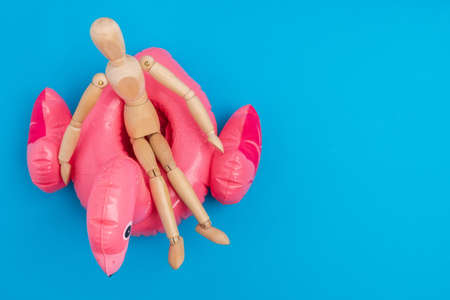 Wooden mannequin on a swimming circle on a blue background. The concept of rest, vacation, copy space for textの写真素材