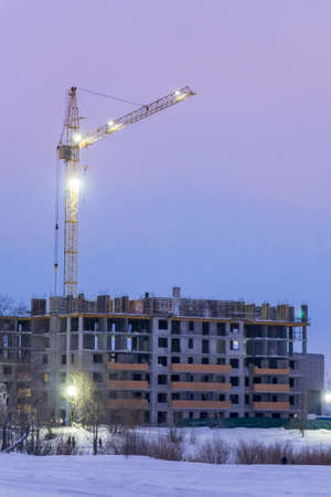 A construction crane in winter next to a building under construction. Vertical photo