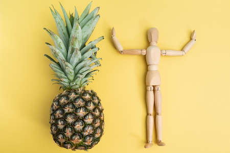 Pineapple on a yellow background with a wooden mannequin. Flat layの写真素材