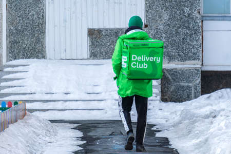 Tyumen, Russia-February 22, 2022: Courier delivery club in uniform and branded green. Thermal bag with symbols and logo of a companyのeditorial素材