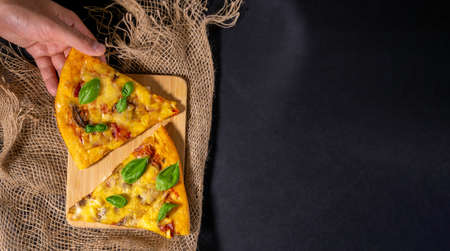 Piece of baked pizza with mushrooms and basil, tomatoes and cheese, black background, flat lay, copy spaceの写真素材