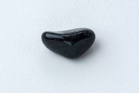 Close up of natural mineral from geological collection tumbled black onyx gem stone, white backgroundの写真素材