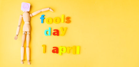 Yellow background with a wooden doll with a smile fools day, April 1. Copy spaceの写真素材