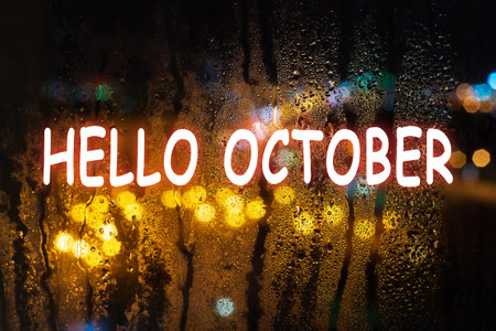 Raindrops on the glass night, the light from the headlights of cars bokeh. Nature background with lettering Hello october.の写真素材