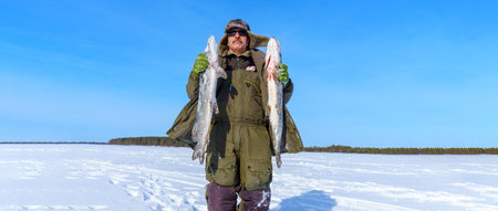 Man Holding a Fish pike in the Snow. Winter fishing, adventure. Banner, copy spaceの写真素材