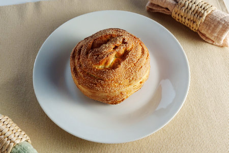 Mouthwatering cinnamon roll takes center stage on a white plate, enticing with its irresistible aroma.の写真素材