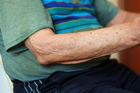 A senior individual wearing a striped shirt sits comfortably at home, absorbed in a calm activityの写真素材