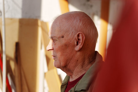 Brilliant sunlight filters through the windows of a craft workshop where an elderly man stands deep in thoughtの写真素材