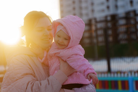 A mother holds her child close under the warm glow of the setting sun in a city park.