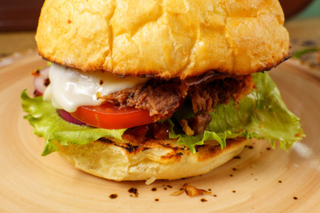 A hearty pulled pork sandwich is prepared with layers of tender meat, fresh lettuce, ripe tomato, and creamy sauceの写真素材