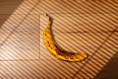 Banana resting on wooden floor with shadow patterns during bright daylightの写真素材