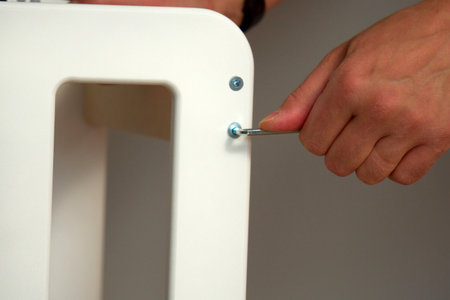 A hand grips a wrench as it tightens a bolt on a white furniture pieceの写真素材