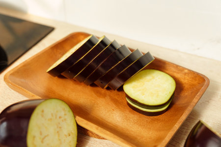 Slicing fresh eggplant on a wooden cutting board in a contemporary kitchen settingの写真素材