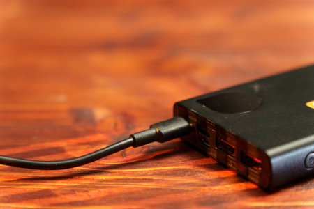 A user plugs a USB cable into a power bank on a wooden surface. The device features multiple portsの写真素材