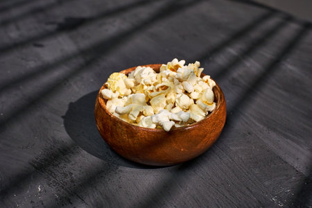 A wooden bowl filled with fluffy popcorn sits on a textured surfaceの写真素材