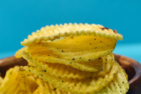 Crisp potato chips are layered in a close-up view, showing their wavy texture and hints of green...