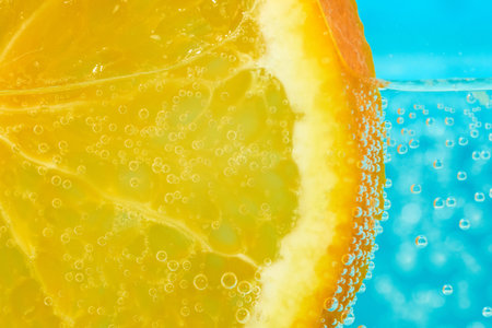 An orange slice is partially submerged in clear sparkling water, creating a refreshing and vibrant...