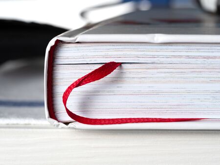 Closed book with a bookmark in the form of a red ribbon close-up. The book is a source of knowledge