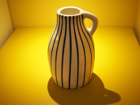 A vase with stripes in a box filled with yellow lightの写真素材