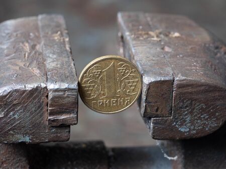hryvnya coin clamped in a metal vise. Currency and Ukrainian economy under the onslaught, the concept of financial problems and crisisの写真素材