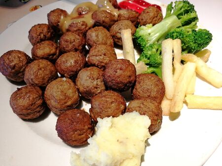 A dish of meat meatballs with side dishes of mashed potatoes, French fries and cooked broccoli