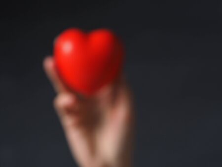 A blurry photo with the outline of a hand holding a red heart. Concept of the day of health, care and medicineの写真素材
