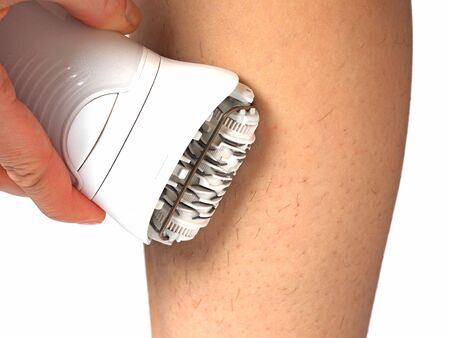 a girl shaves her leg with an electric epilator on a white background. Concept of women's beauty and foot skin care.の写真素材