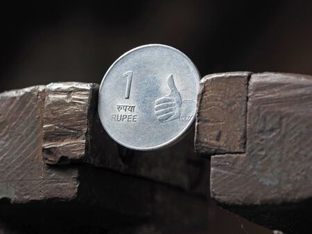 Indian rupee coin clamped in a metal vise on both sides. The concept of financial pressure on the currency businessの写真素材