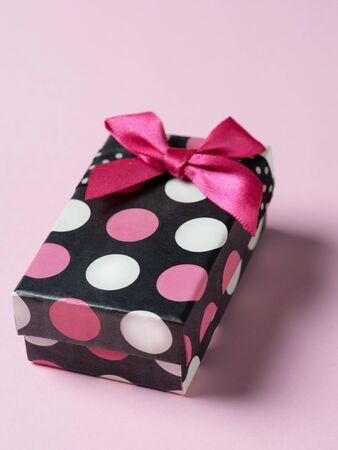 colorful gift box in colorful polka dots with a bow lies on a pink backgroundの写真素材