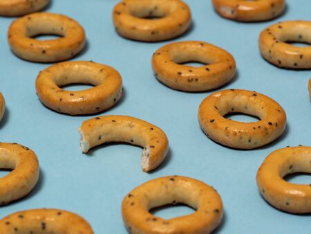 Pattern of edible products. bagels with poppy seeds lie on a blue paper background. One of them is different from the othersの写真素材