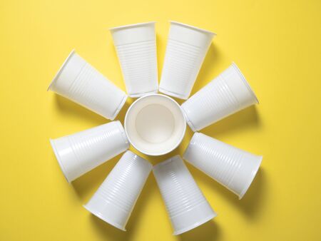 white disposable cups stand on a yellow background laid out in the shape of the sun