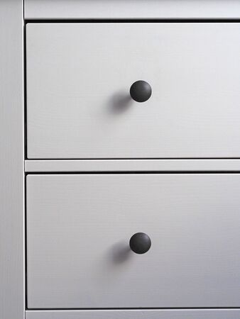 close-up of a modern white wooden chest of drawers with black handles. Minimalism, modern interior