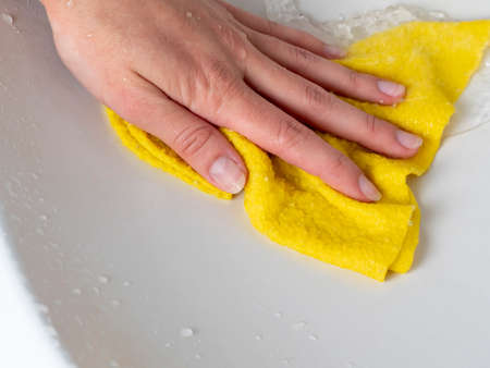 a woman's hand with a yellow cloth washes the sink. The concept of cleaning the houseの写真素材